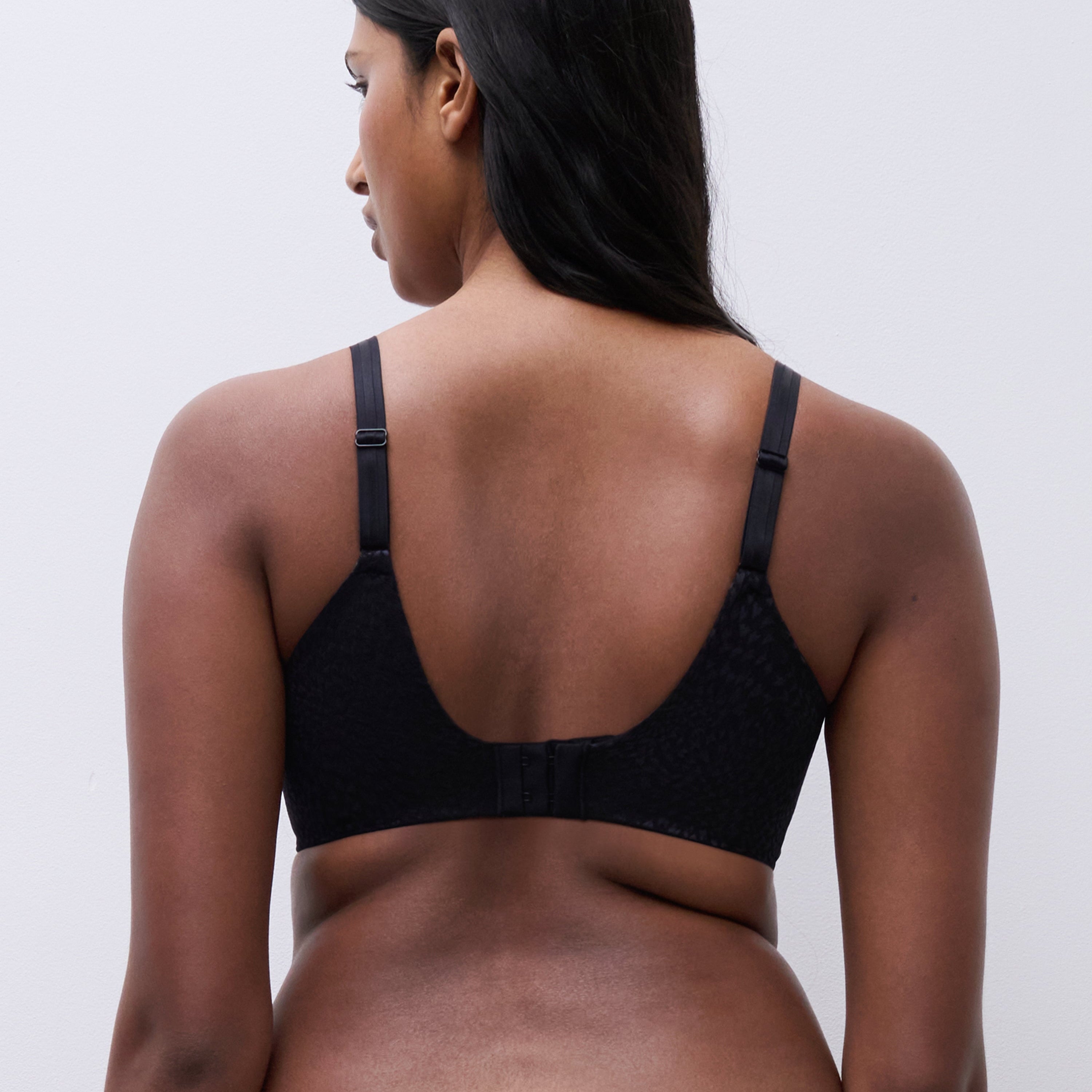 Back view of a woman wearing the Magique minimizer bra in black, showing the tall U-shaped back and smoothing band