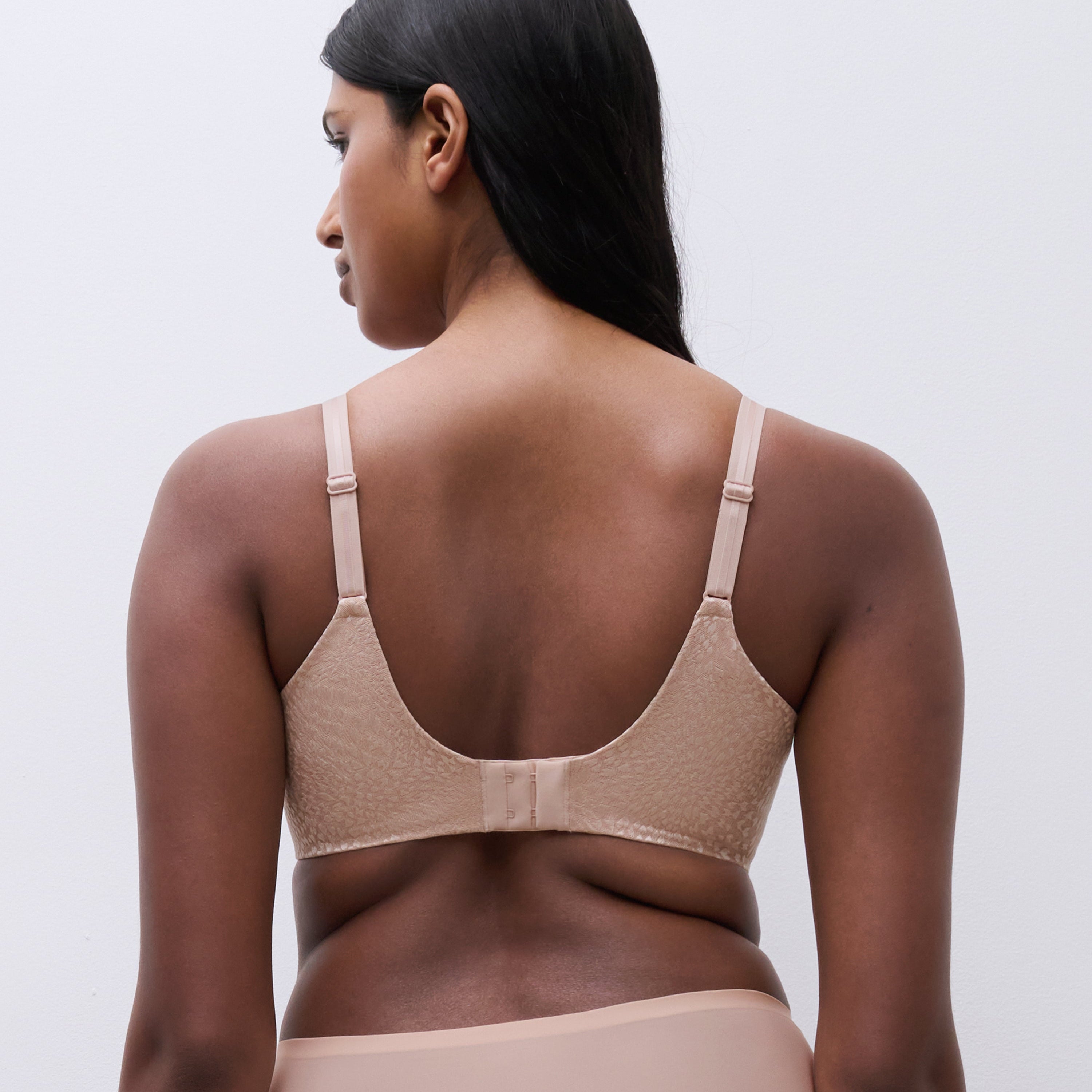 Back view of a woman wearing the Magique minimizer bra in rose, highlighting the smoothing back band and adjustable straps